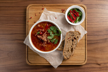 A bowl of borscht - a traditional Ukrainian soup made from beets, vegetables and meat with bread on a wooden table. Top view.