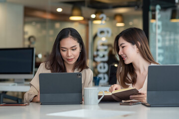 Charming Asian businesswoman working together using a tablet and taking notes at the office.