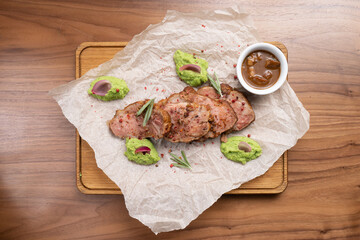 Pieces of roast pork with spices, rosemary, pea puree and sauce on a wooden table