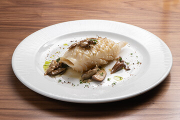 Beautifully cooked fried squid carcass with wild mushrooms and herbs in a white plate on a wooden table.