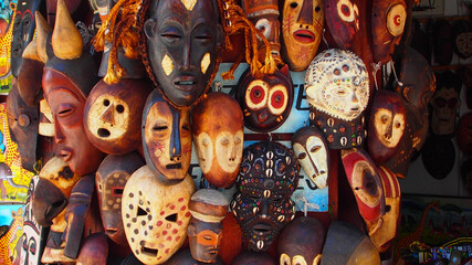 Selection of African masks carved from wood and decorated, some with seashells and others by being engraved - obrazy, fototapety, plakaty