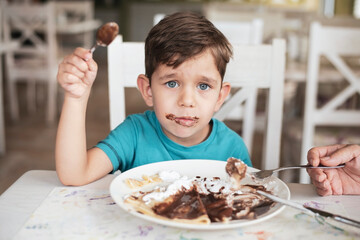 The little boy in the cafe eats a delicious dessert, pancakes with cream, but a boy has a bad...