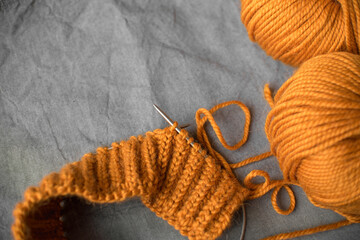 Obraz na płótnie Canvas bright balls of orange woolen thick yarn and knitting on a gray wrinkled background with place for text
