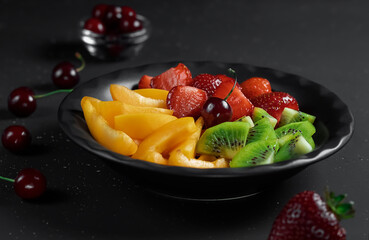 Summer diet salad served in portions in a black plate. Selective focus on sweet cherries in a plate. Black background