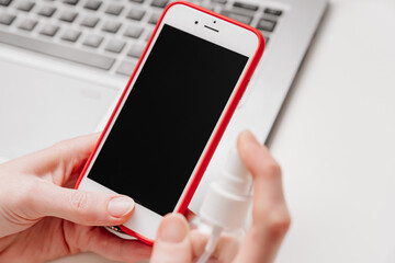 Smartphone screen is treated with antiseptic or cleansing spray for electronics.