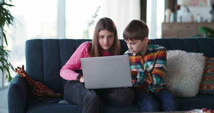 Couple of caucasian cute children using laptop computer connecting internet social media typing messages and watching fun vifdeo content together.