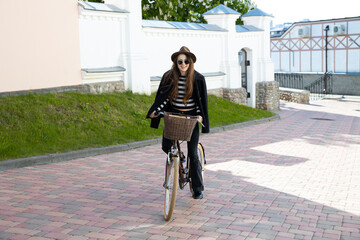 Fototapeta premium Young woman in a hat and glasses riding a bike around the city