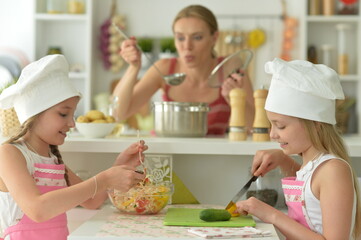 Cute girls with mother  preparing delicious fresh salad in kitchen