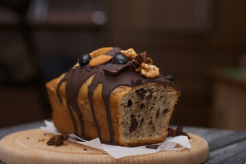 Banana bread garnished with nuts and dried fruits. A slice of bread is visible. Close-up shot.