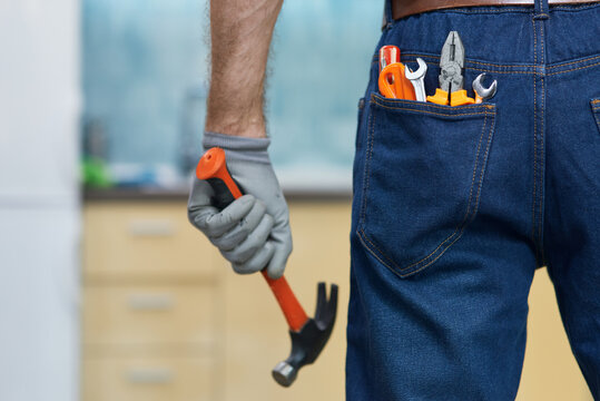 Nail it. Close up shot of various plumbing hand tools in man's jeans back pocket. Professional repairman holding a hammer, standing indoors