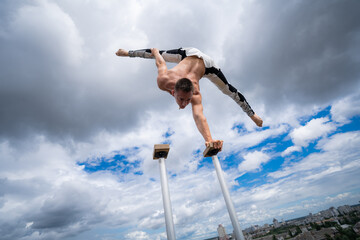 Flexible male circus Artist keep balance by one hand against amazing cloudscape. Individuality,...