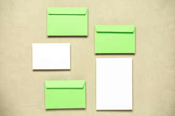 Blank paper card and green envelopes on a concrete beige background. Modern stationery scene. Template for your design. Top view, flat lay.
