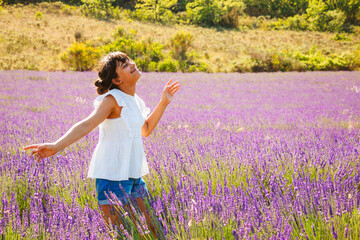 Happy girl enjoying the sun and the aroma in a french lavender field