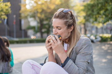 stylish hipster woman eating juicy burger.  girl biting yummy cheeseburger on the street in city. street food festival. summertime. 