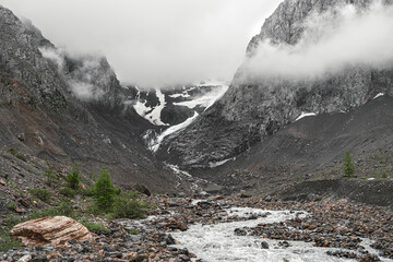 A glacier in a gorge between the mountains, from which a river flows. Beautiful alpine landscape...