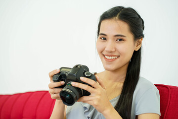 Asian young pretty attractive  woman model in photographing shooting studio sitting on red couch and lookin to digital camera white background