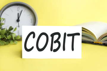 COBIT. text on white paper on a yellow background near the pen.