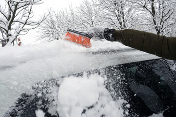 Removing snow from car with a brush. Man cleans his car after a snowstorm.