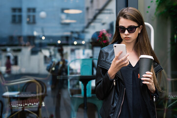 Concentrated woman with coffee and smartphone standing in street