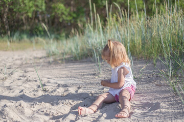 Little girl at the beach, summer dressed child girl sit down on sand beach playing smiling with sand, warm colours