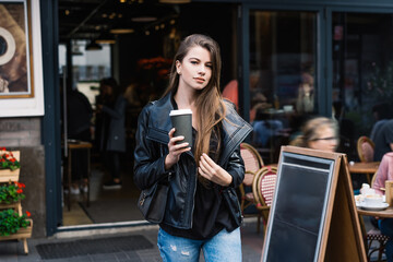 Pleasant young female with hot takeaway beverage leaving cafe