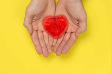 Obraz premium Men's hands are holding a red heart on a yellow background. Love, relationship concept. Romantic symbol, gift card for Valentine's Day.