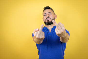 Handsome man with beard wearing blue polo shirt over yellow background showing middle finger doing...