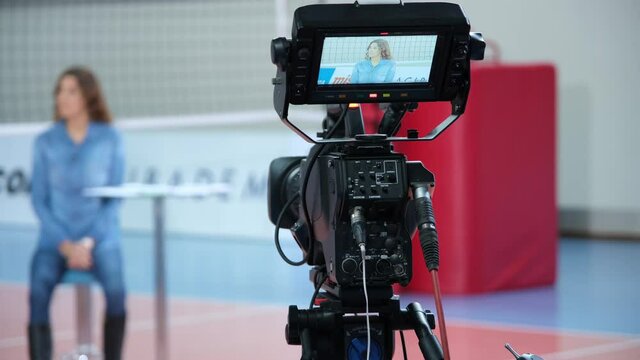 The young woman, who is a presenter on a TV show, appears from the viewfinder of the professional camera.