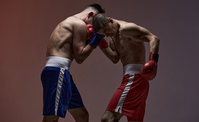 Battle of boxers two fighting males in boxing gloves in red studio light, martial arts, mixed fight...