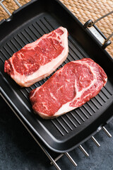 Raw rib eye and striploin New York beef steak on black grilling pan, top view.