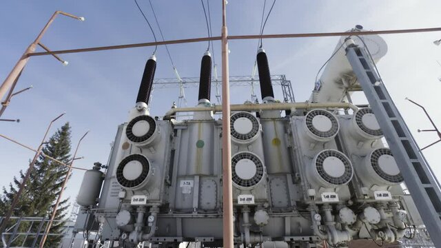  High voltage electrical substation on blue cloudy sky background. Action. Bottom view of a transformer near street lamps, concept of energy system.