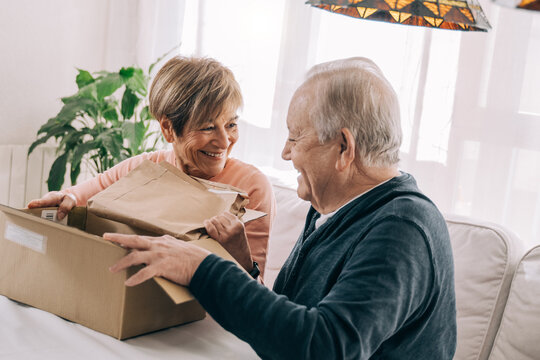 Happy senior couple opening package received from online delivery at home - Elderly people and technology trends concept - Focus on parcel box