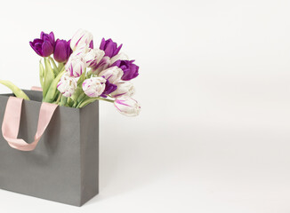 Tulips in a gift bag on a white background. Postcard for March 8, Mother's Day, birthday. Flower delivery. Flower Shop. Space for text