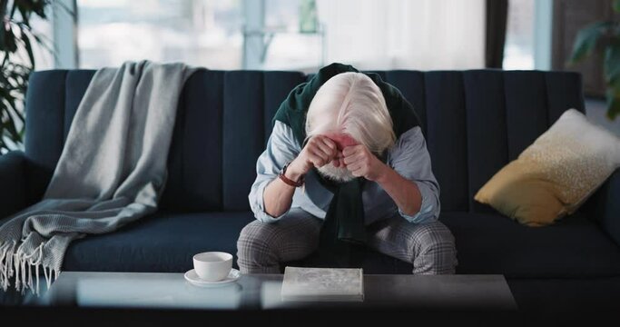Bearded lonely caucasian old man watching TV failed football game frustrating about loss crying on the sofa. Home entertainment. Football fan.