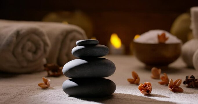 Spa salon equipment. Close up shot of massage hot stones with little flowers around and towels with flaming candles on background - wellness, spa concept 4k footage