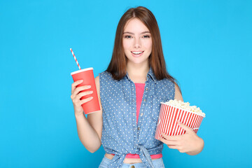Beautiful girl with bucket of popcorn and drink on blue background