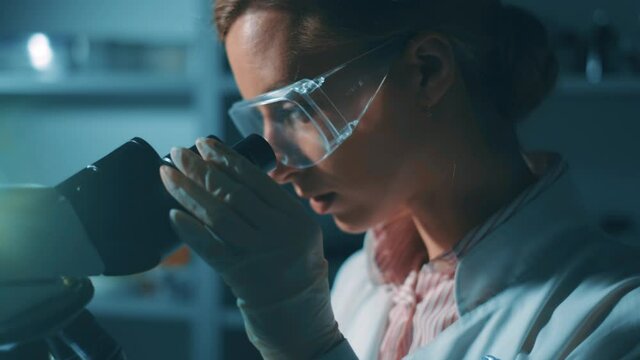 A woman scientist is looking into microscope, biochemical research. Scientific and medical lab instrument. A doctor is search for vaccine to treat diseases in laboratory for medicine study