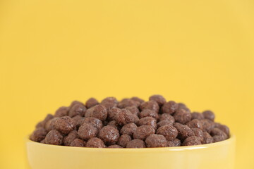 Chocolate cereal corn balls in a yellow bowl on a yellow background. Copy, empty space for text
