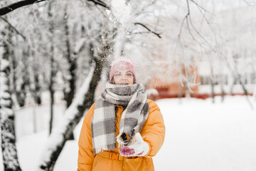 Blurred background. Beauty winter girl blowing snow in frosty winter park. Outside. Flying snowflakes. Sunny day. Backlight. Joyful beauty young woman having fun in winter park