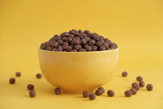 Chocolate cereal corn balls in a yellow bowl scattered on a yellow background. Copy, empty space for text