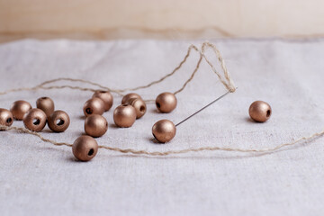 Large beads coated with bronze paint are strung on the needle. Materials for creativity and needlework at home. Old homespun tablecloth.