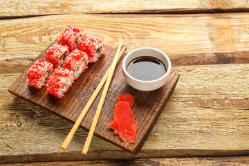 Roll with shrimp cucumber and tobiko caviar and sticks on a board and soy sauce in a sauce bowl on a wooden background.