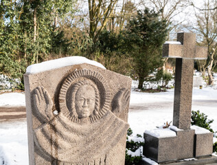 schöner Grabstein und ein Kreuz auf verschneitem Friedhof