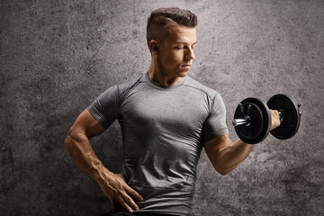Fototapeta premium Bodybuilder exercising with a dumbbell and leaning on a rusty wall
