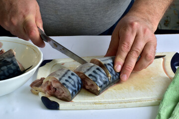 A man's hands with a knife with a wide blade cuts the fish into pieces.