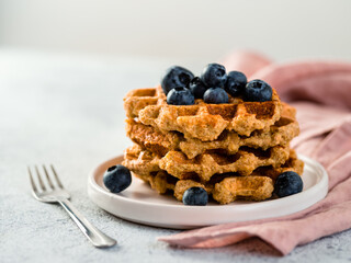 Easy healthy gluten free oat waffles with copy space. Stack of appetizing homemade waffles with oat flour decorated blueberries, on plate over light gray cement background