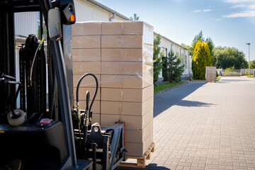 Forklift vehicle manipulating goods in logistic area outside warehouse.