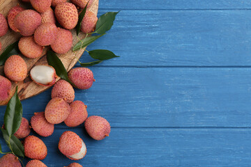 Fresh ripe lychee fruits on blue wooden table, flat lay. Space for text