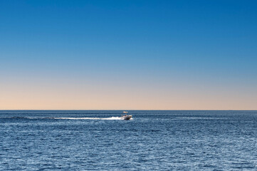 A lonely motor boat sails in the sea. Lonely boat, movement on the water. Calm water surface with horizon line background