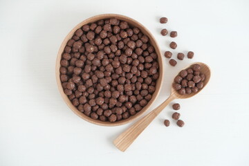 Chocolate corn balls in a wooden bowl and spoon scattered on a white background. Top view. Copy, empty space for text